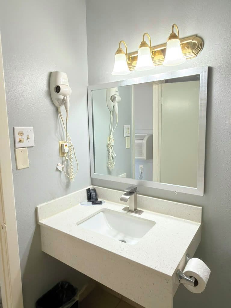 Une salle de bain avec un lavabo blanc, un miroir, un sèche-cheveux et un miroir de coiffeuse avec éclairage.