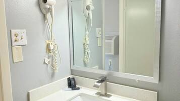 A bathroom with a white sink, a mirror, a hairdryer, and a lighted vanity mirror.