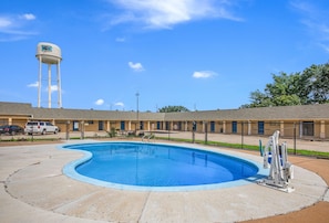 Una piscina con una torre de agua al fondo, rodeada por un motel de diseño sencillo y funcional.