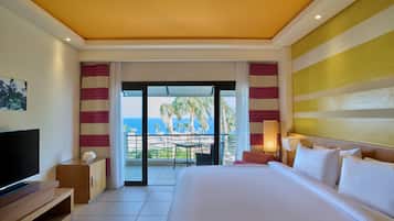 Habitación de hotel con una cama grande, televisión, balcón y vistas al océano, además de cortinas a rayas.