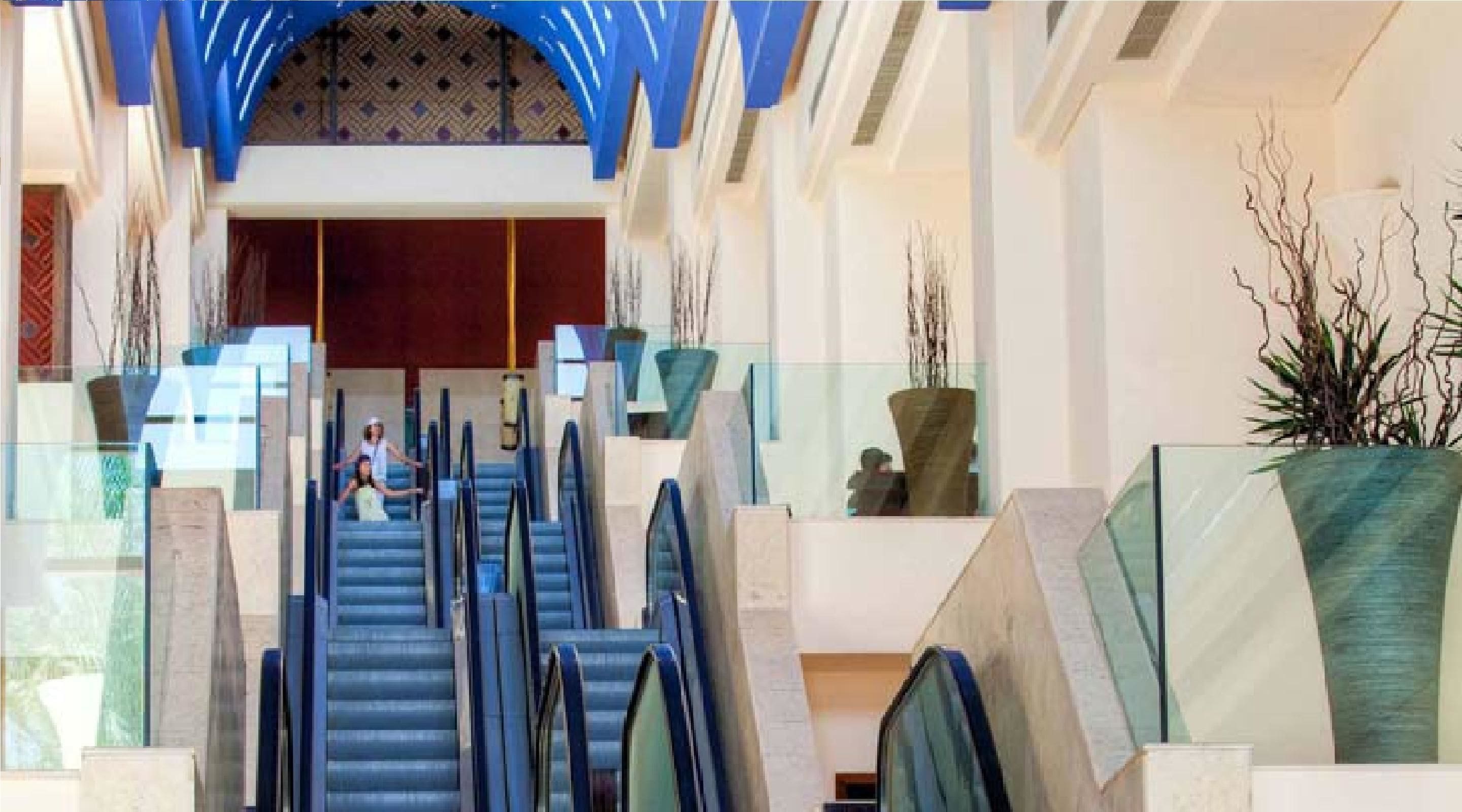 A grand staircase in a hotel lobby with glass railings and decorative plants.