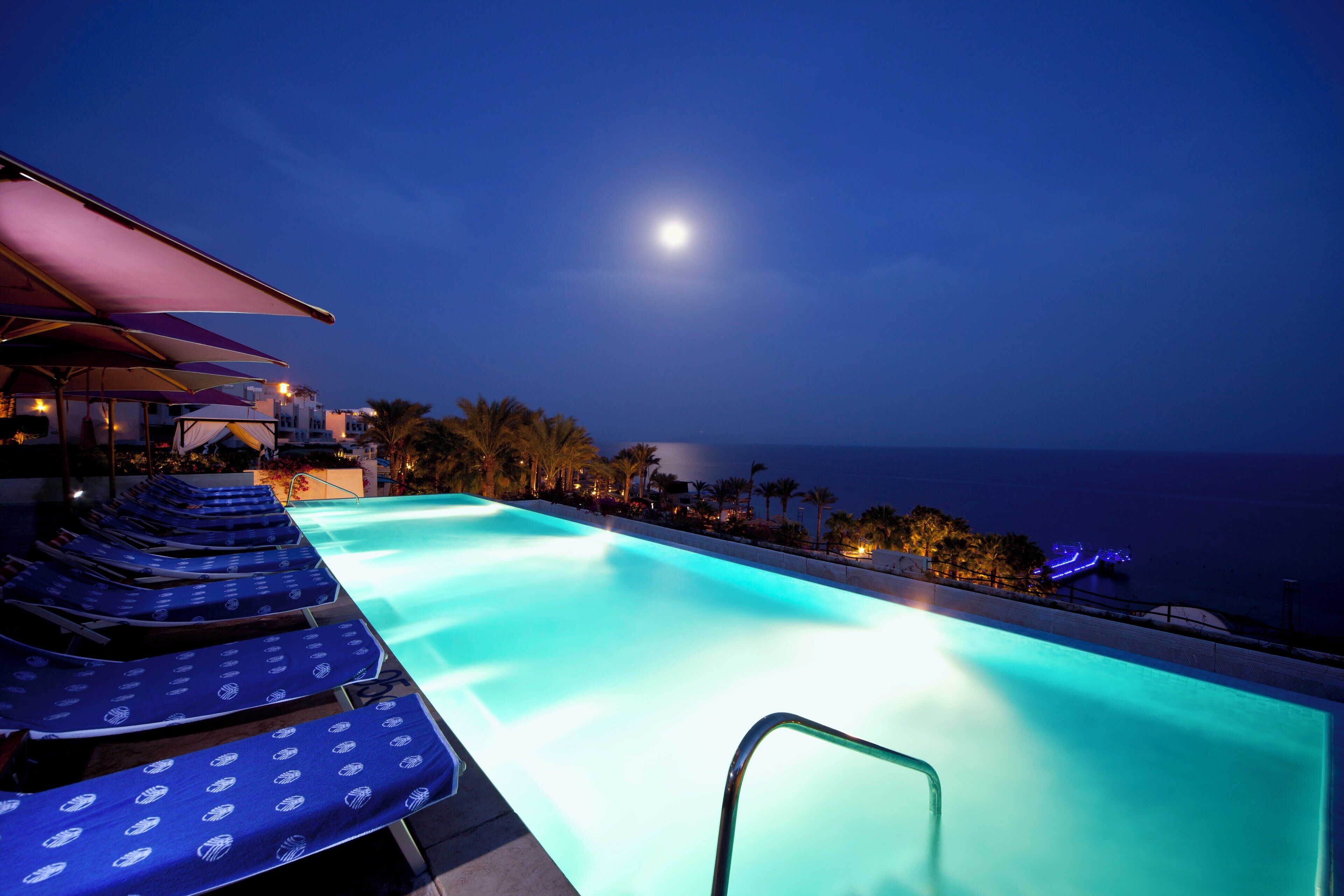 A poolside area with lounge chairs and a view of the ocean at night.