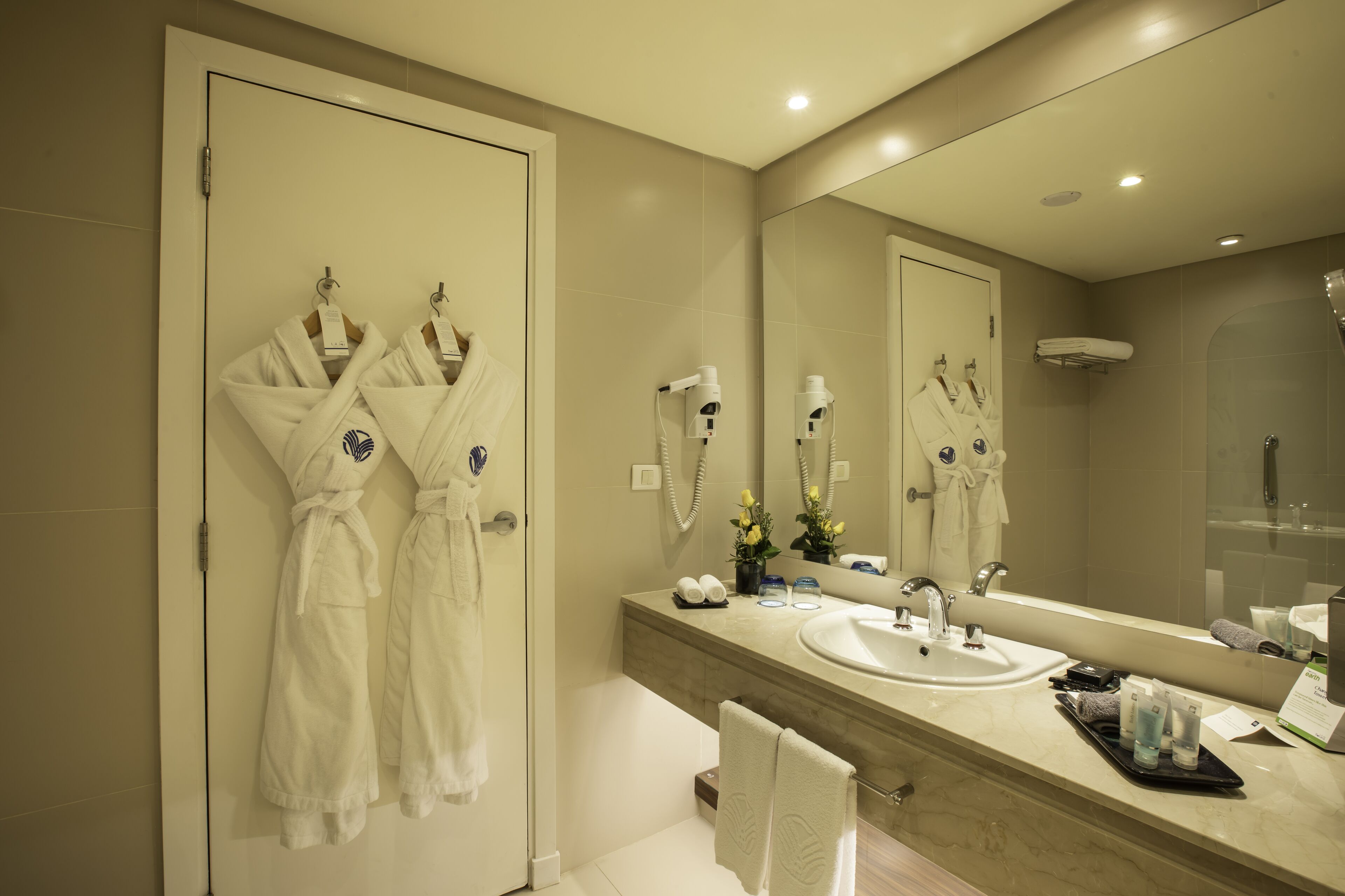 A modern bathroom with a large mirror, a sink, and two robes hanging on the wall.