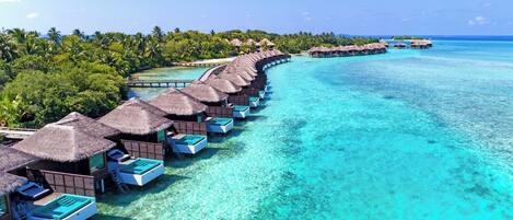 An aerial view of overwater bungalows with clear turquoise waters and lush greenery.