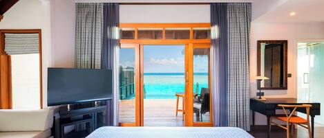 A hotel room with a large bed, a TV, a desk, and a view of the ocean.