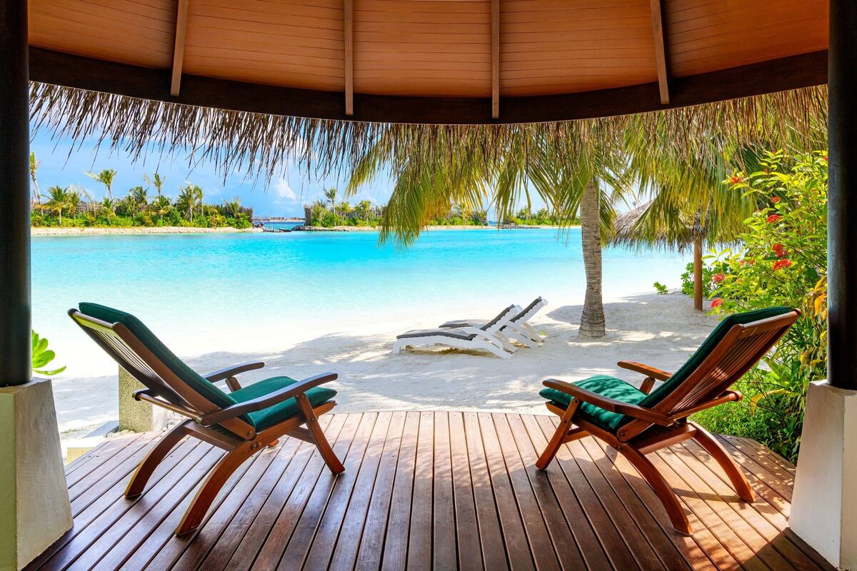 A wooden deck with two lounge chairs facing a beach and ocean view.