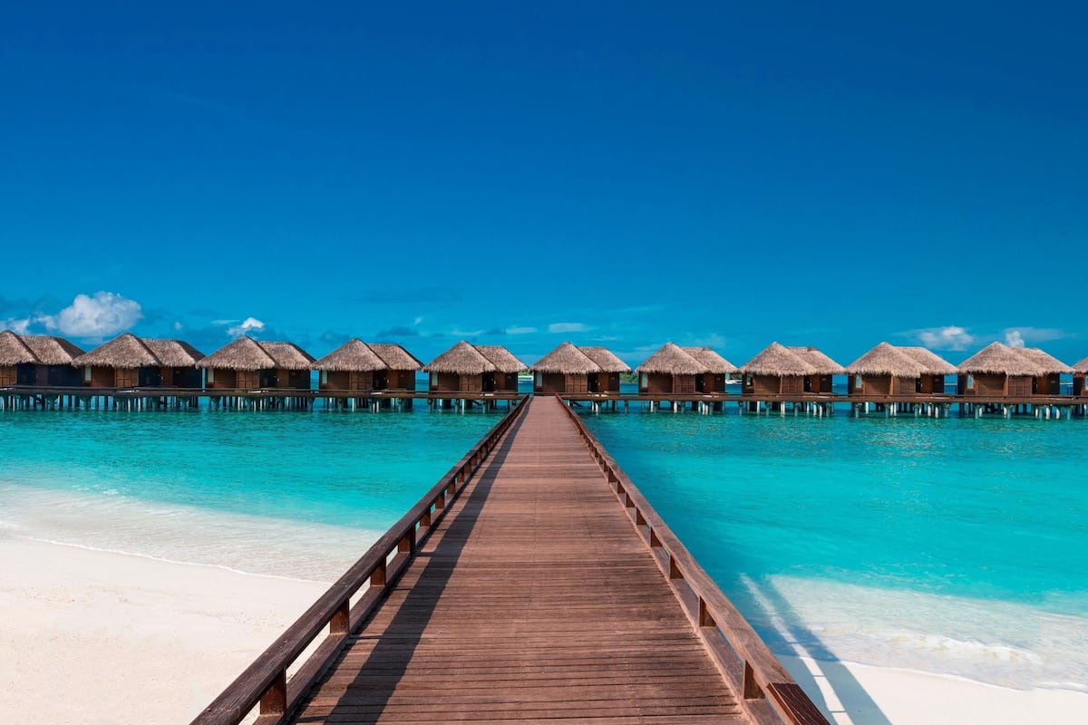 A wooden pier leading to overwater bungalows with thatched roofs, surrounded by turquoise waters.