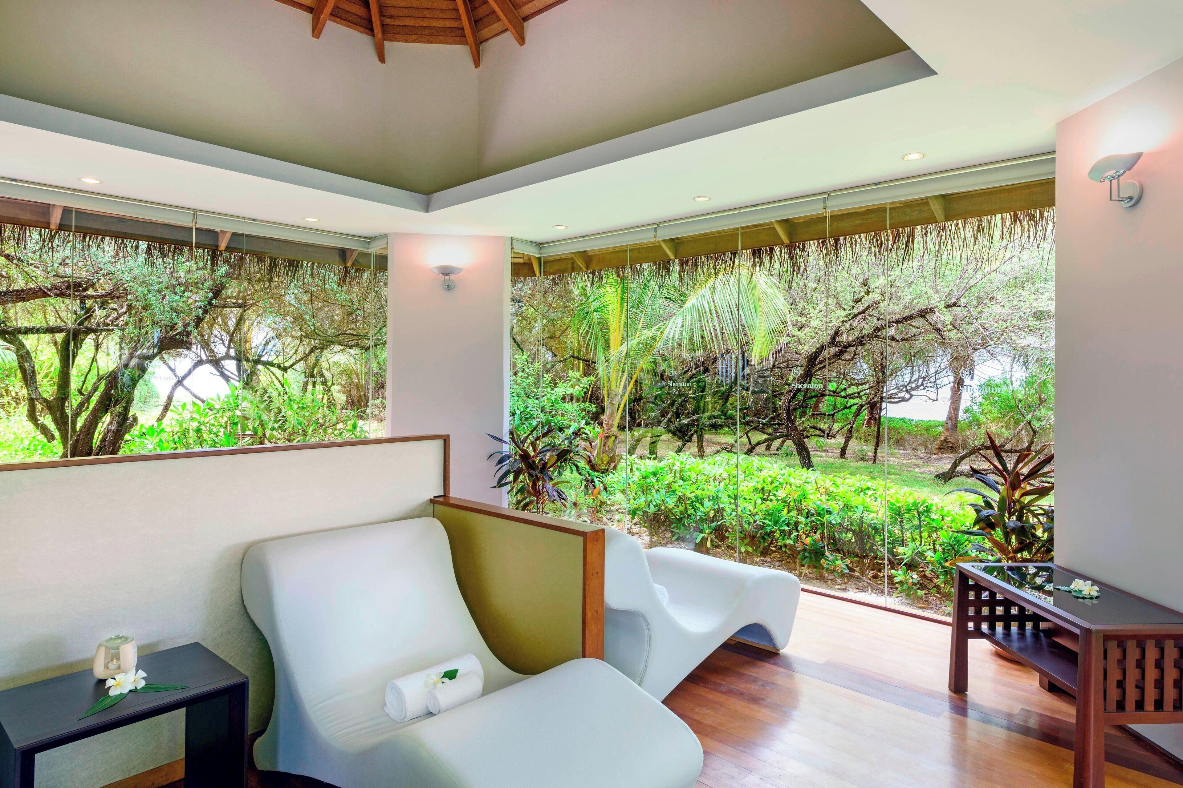 A modern room with a large window overlooking a lush garden. There is a white sofa and a small table with a decorative item.