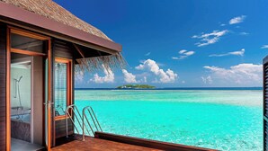 A wooden deck with a glass door leading to a bathroom, a towel on a white mat, and a view of turquoise waters and an island. - Sheraton Maldives Full Moon Resort & Spa (Furanafushi Island)