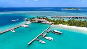 An overwater bungalows with a pier, boats, and a small island in the background. - Sheraton Maldives Full Moon Resort & Spa (Furanafushi Island)
