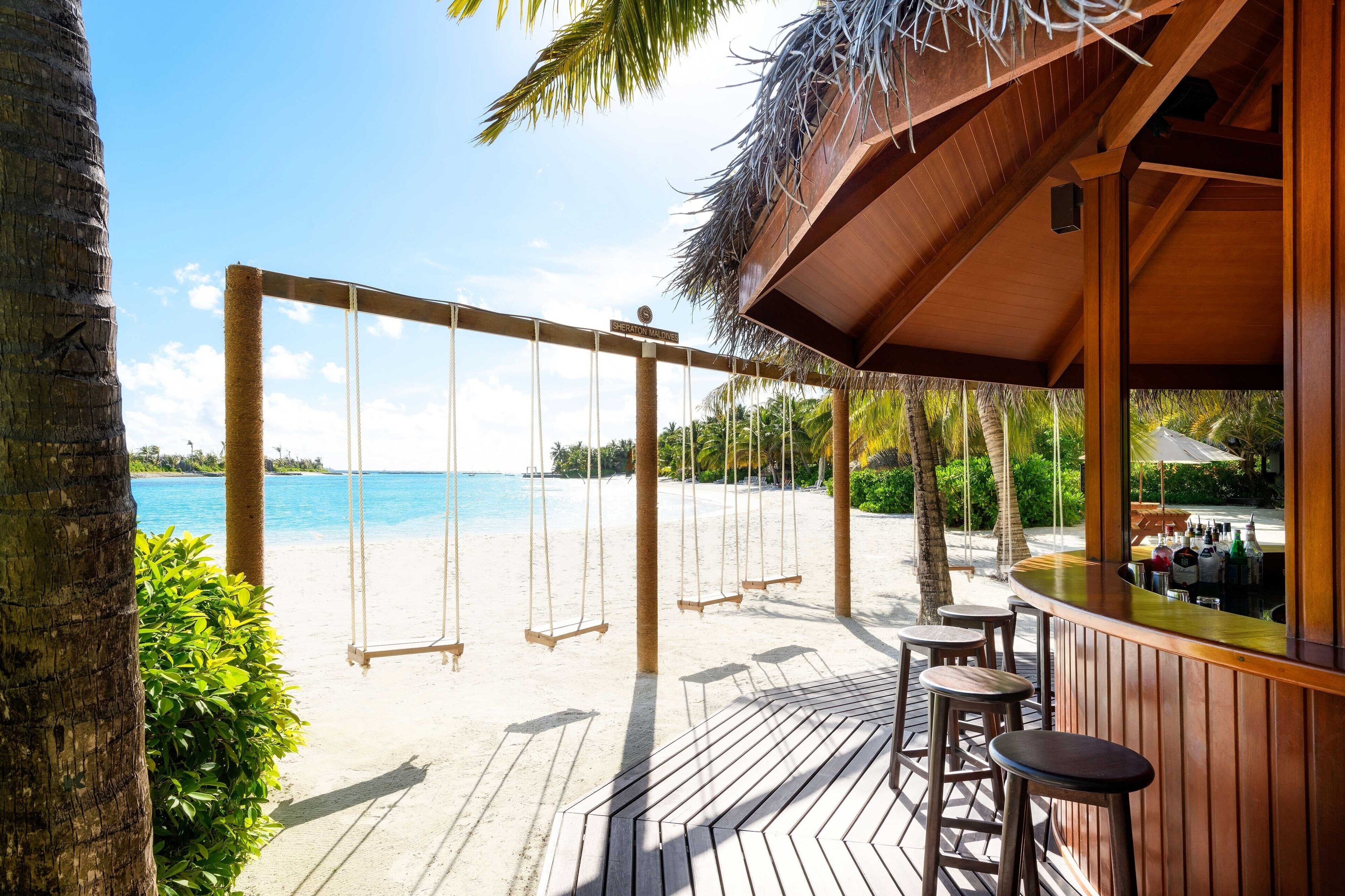 A beachside bar with swings overlooking the ocean.