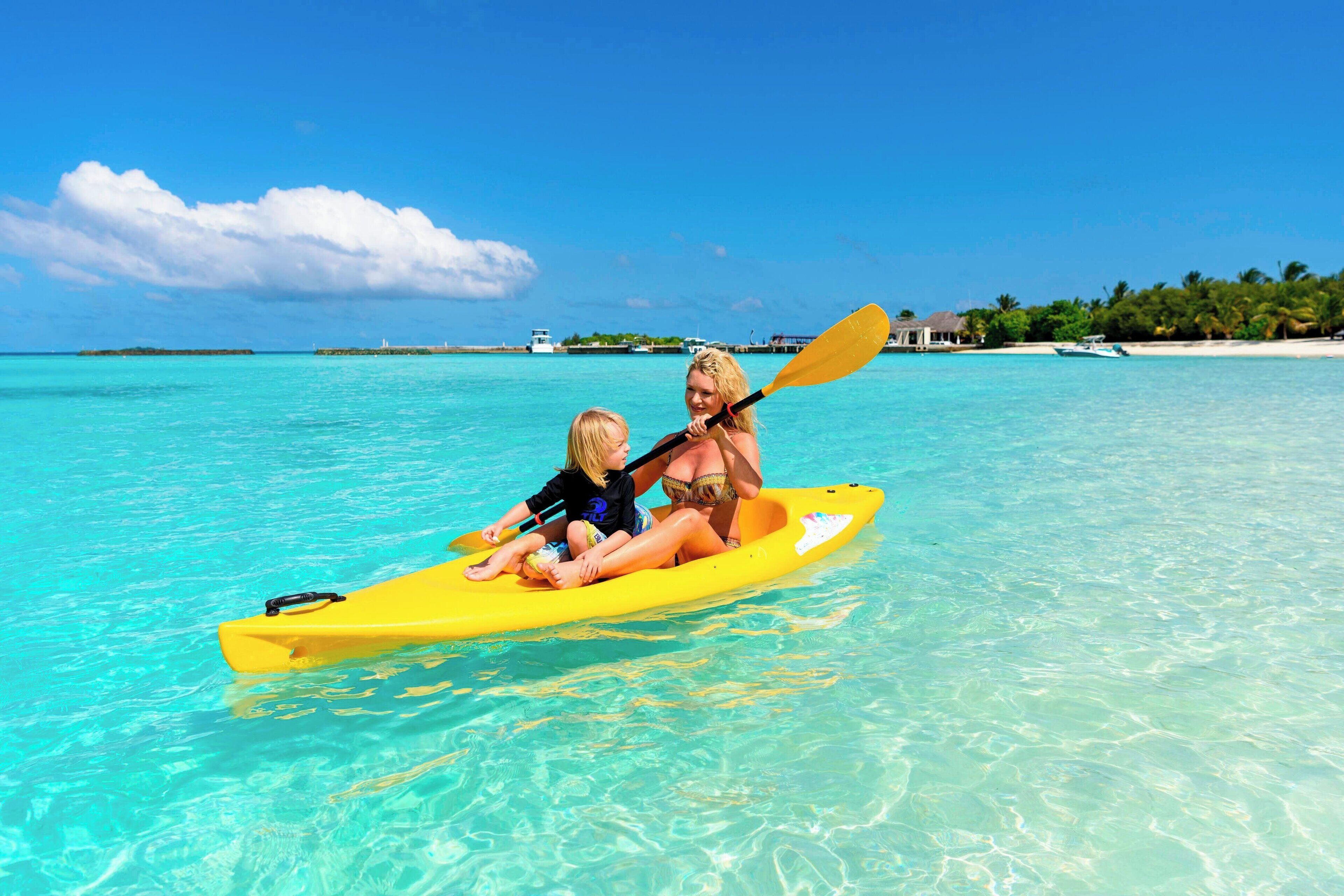 A couple in a yellow kayak on clear turquoise water with a tropical backdrop.