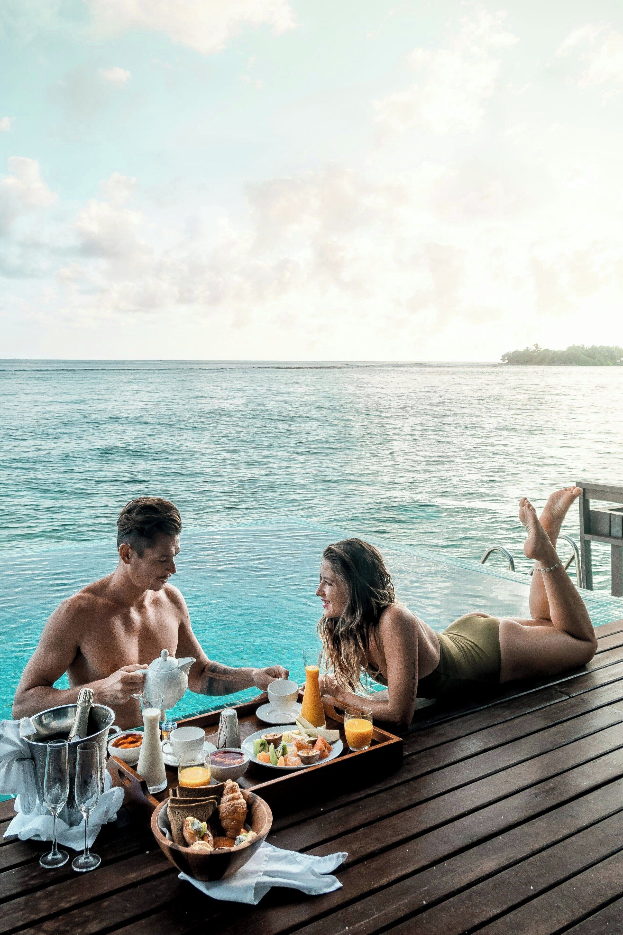 A couple dining by a pool with a view of the sea.
