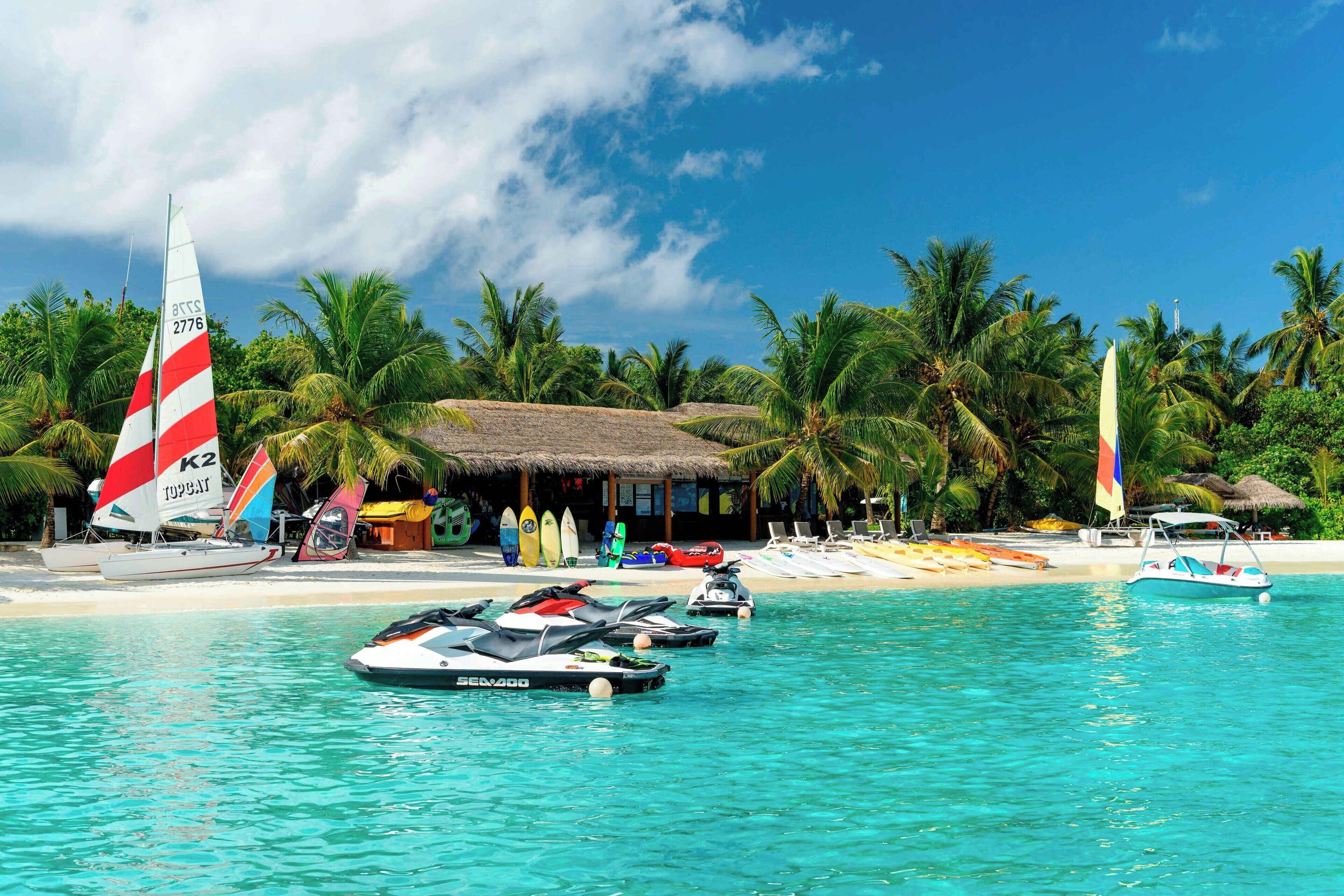 A beachside resort with a clear blue pool, several boats, and palm trees.
