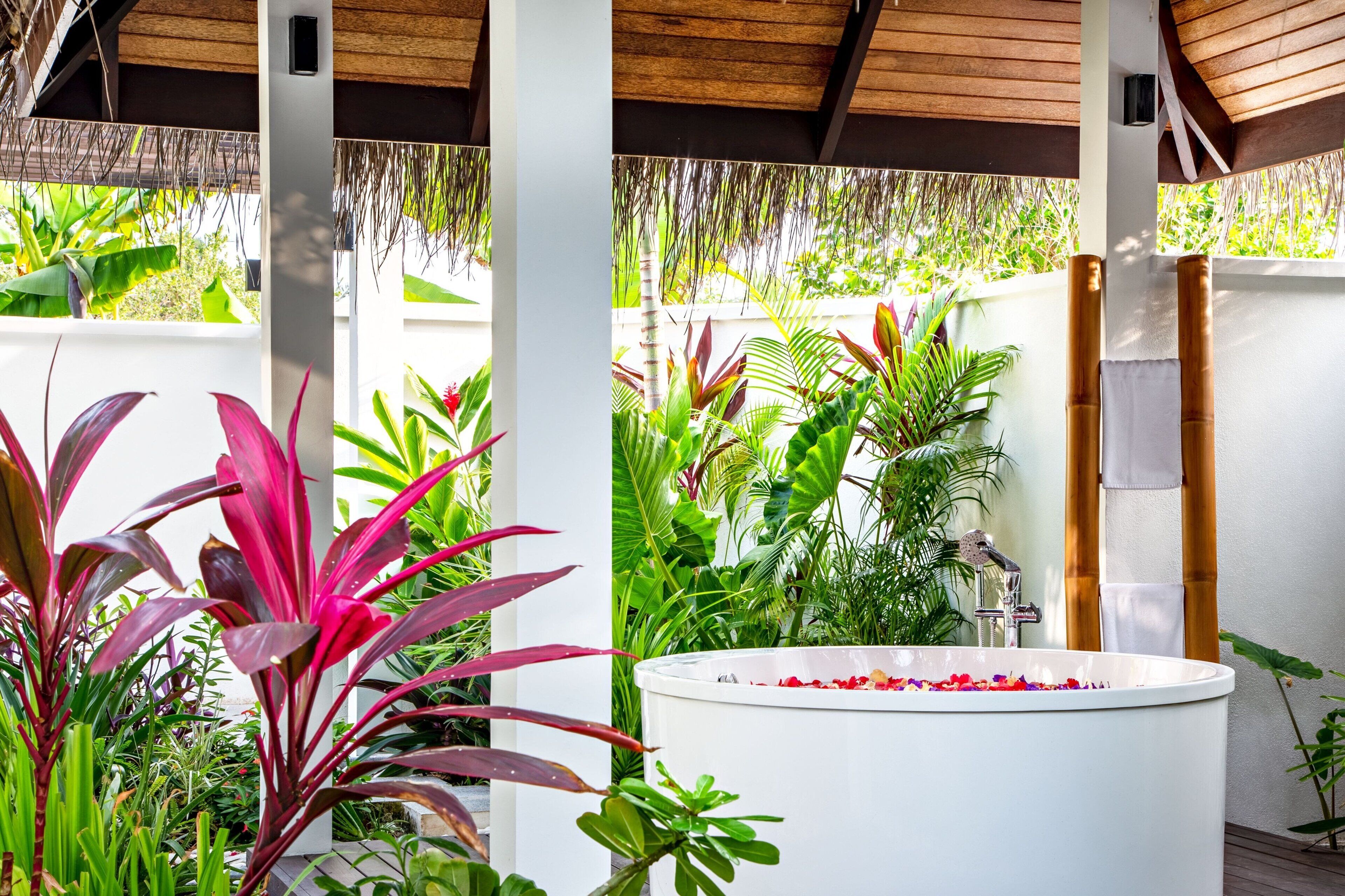 Un espace de bien-être avec une baignoire blanche entourée d’une végétation tropicale luxuriante.