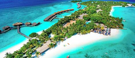 An aerial view of a tropical resort with overwater bungalows, a white sandy beach, and clear turquoise waters.