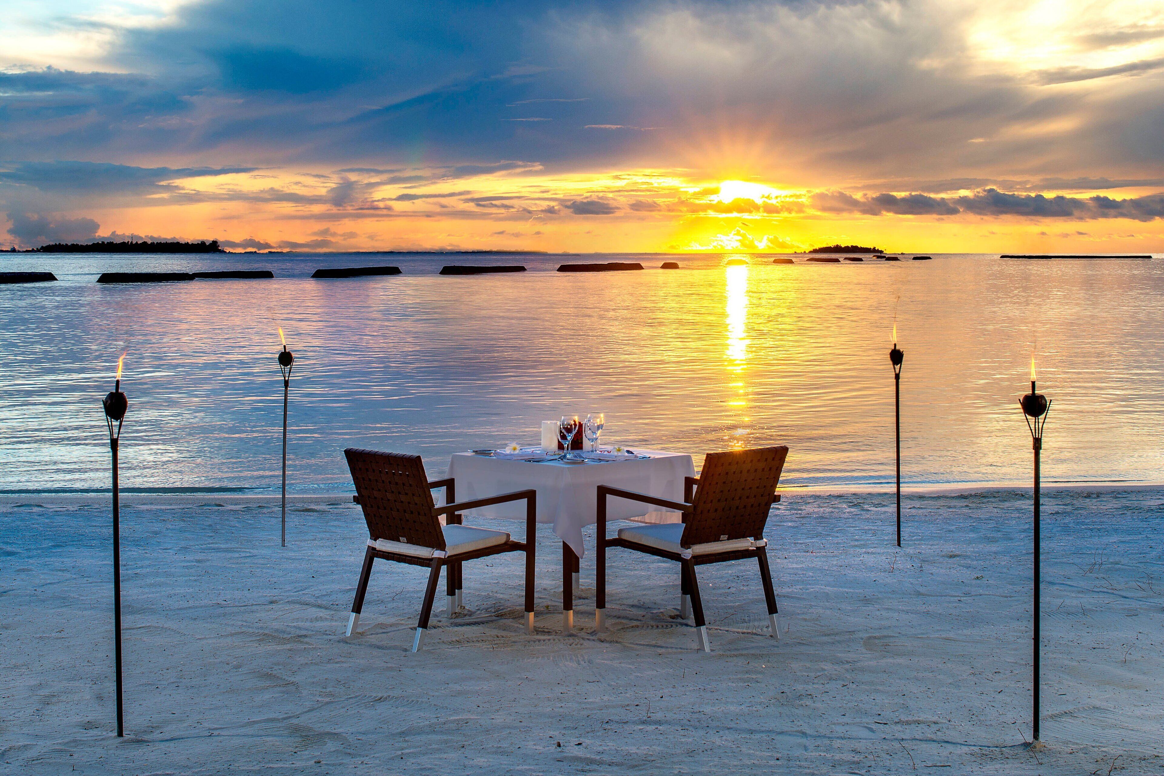 Mesa para dos en una playa arenosa con vista al atardecer.