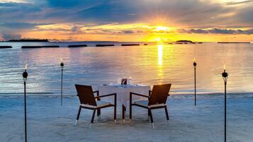 Mesa para dos en una playa arenosa con vista al atardecer.