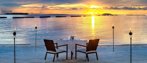 Mesa para dos en una playa arenosa con vista al atardecer.