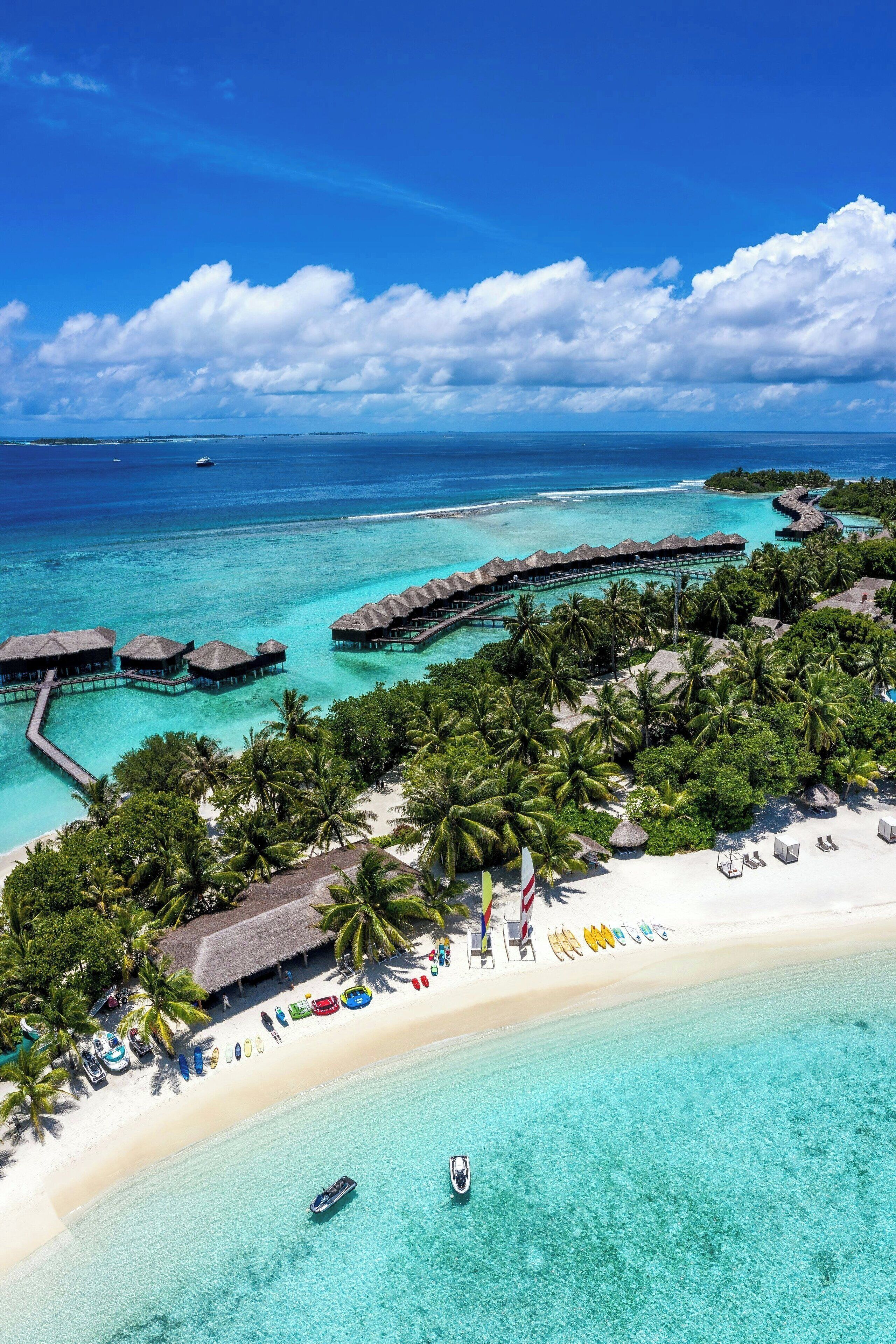 An aerial view of a tropical resort with overwater bungalows, a beach, and clear turquoise waters.