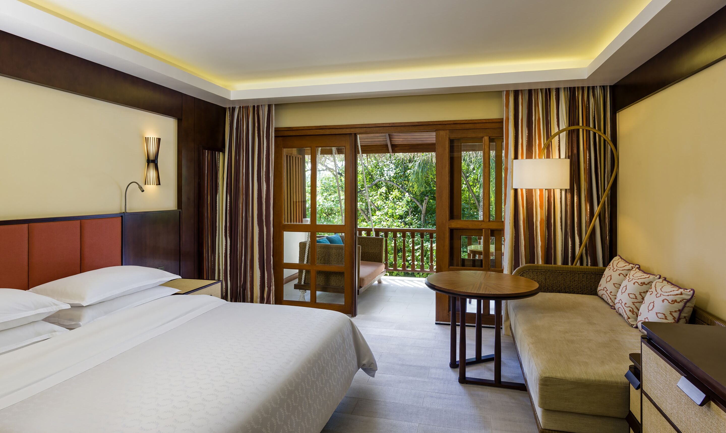 A hotel room with two beds, a sofa, a small table, and a balcony with curtains.