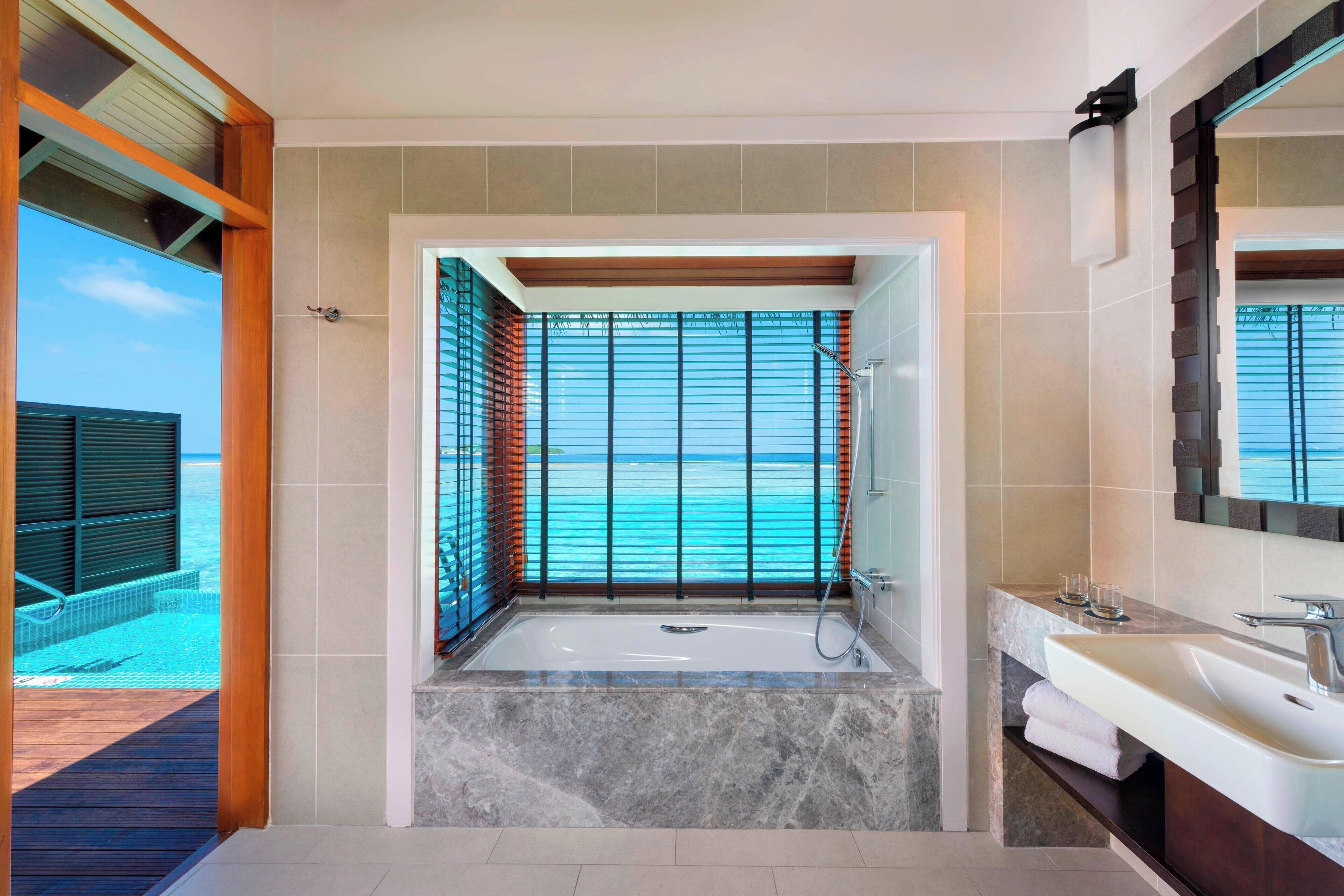 Un baño moderno con una bañera grande, un tocador con espejo y vistas al océano.