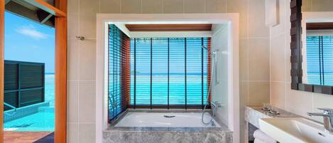 Un baño moderno con una bañera grande, un tocador con espejo y vistas al océano.