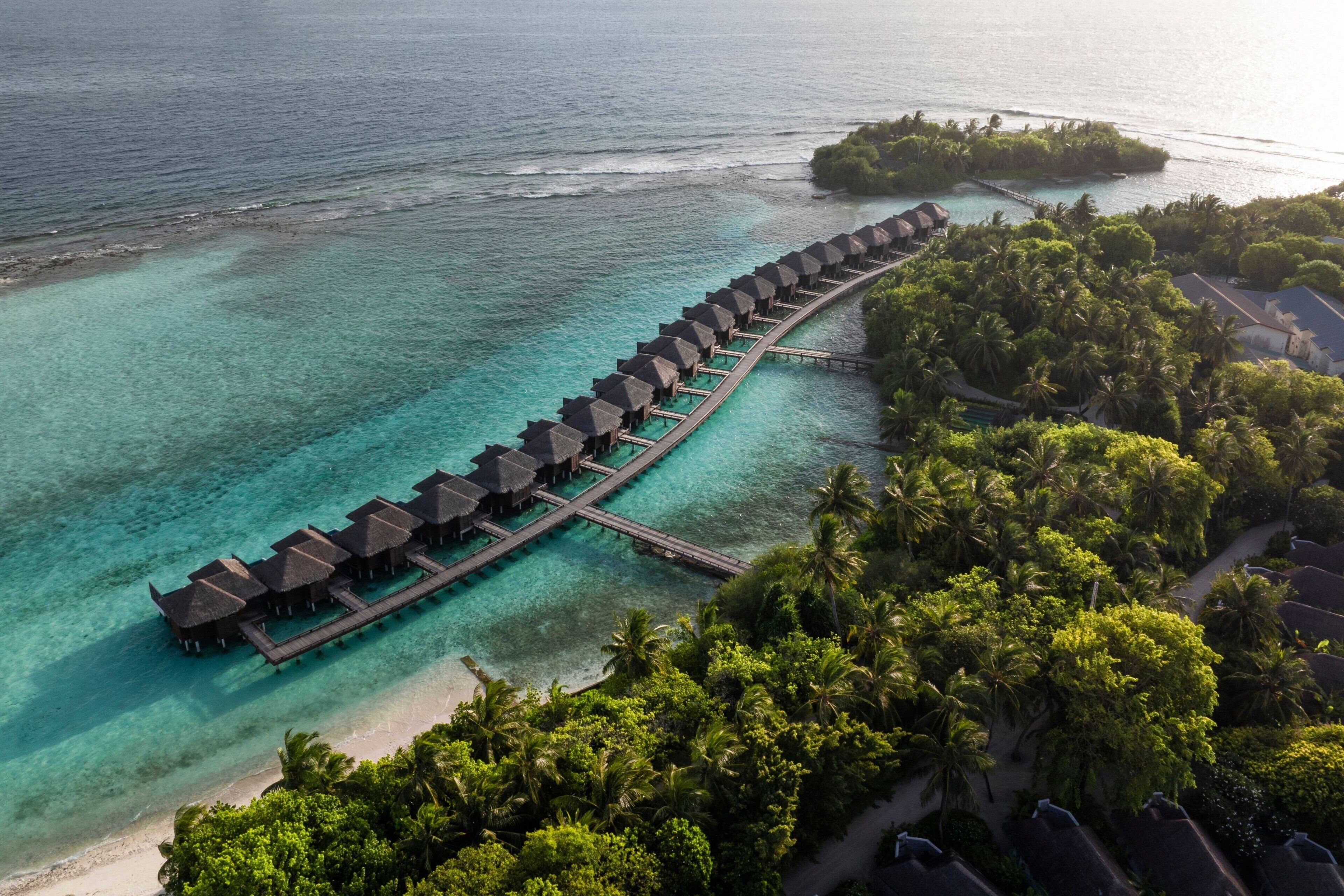 Un resort con bungalow sull'acqua, caratterizzato da diversi livelli di costruzioni a tetto di paglia collegate da passerelle.