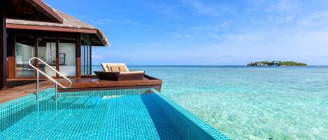 An infinity pool with clear blue water, a wooden deck, and a lounge chair.