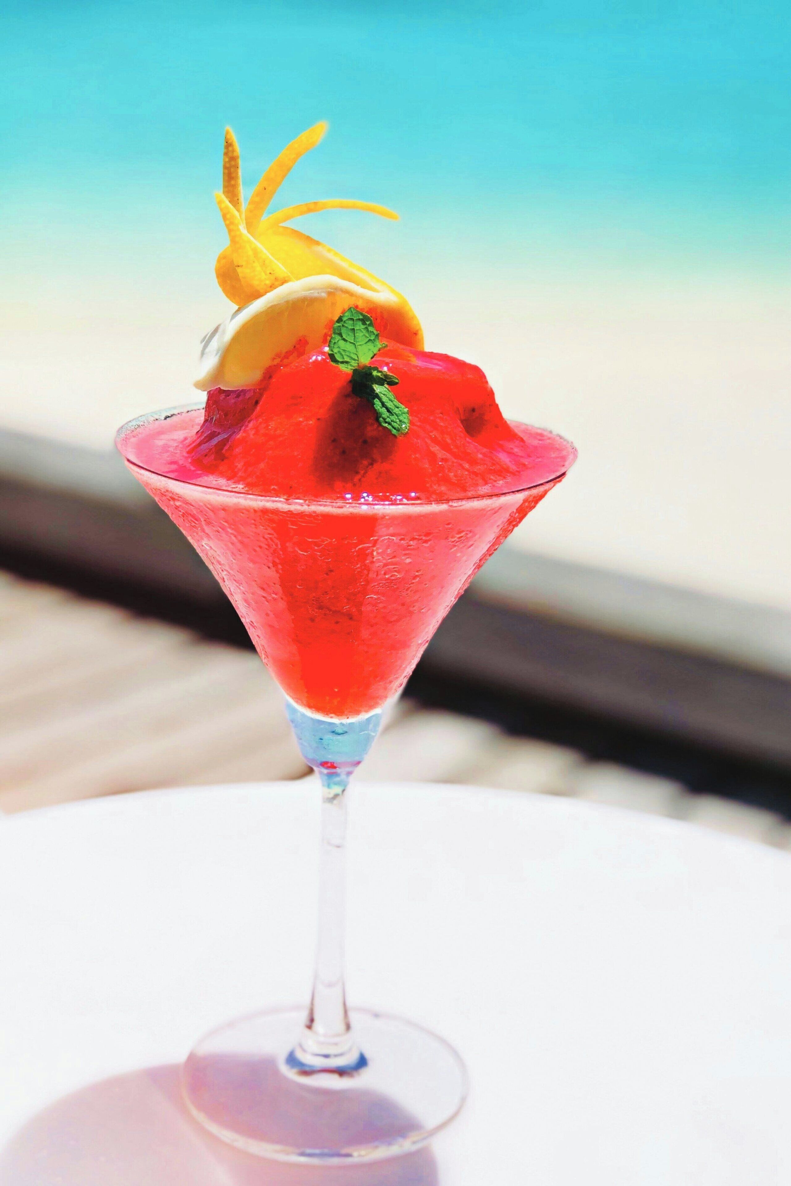 A cocktail in a martini glass with a tropical garnish, set against a beach backdrop.