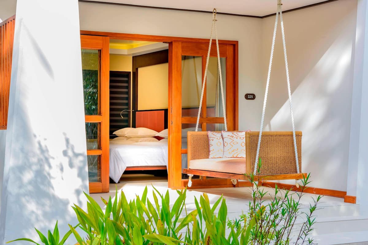 A modern bedroom with a bed, a hanging chair, and a view of the outside.
