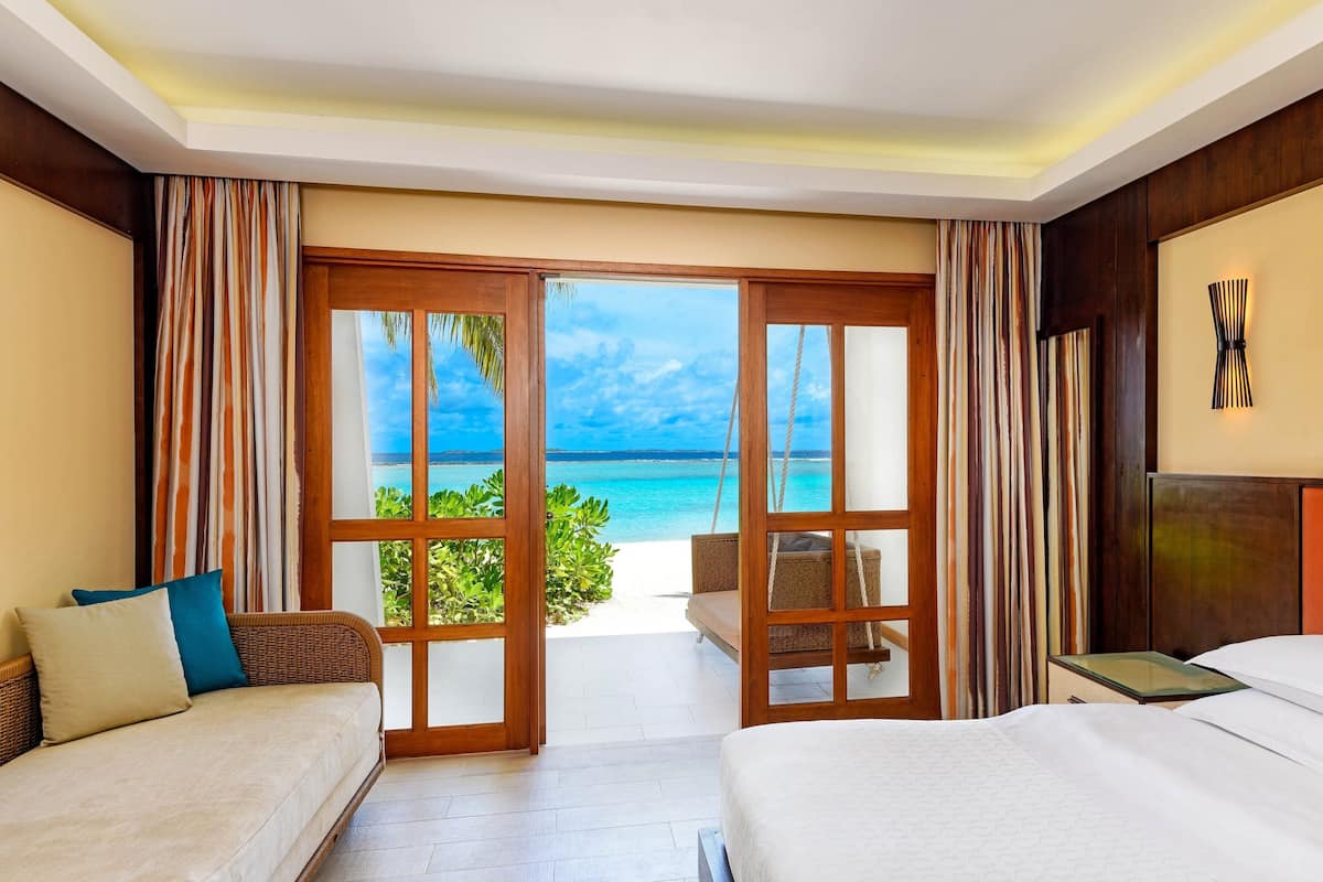 A hotel room with a bed, a sofa, a nightstand, and a view of the ocean.