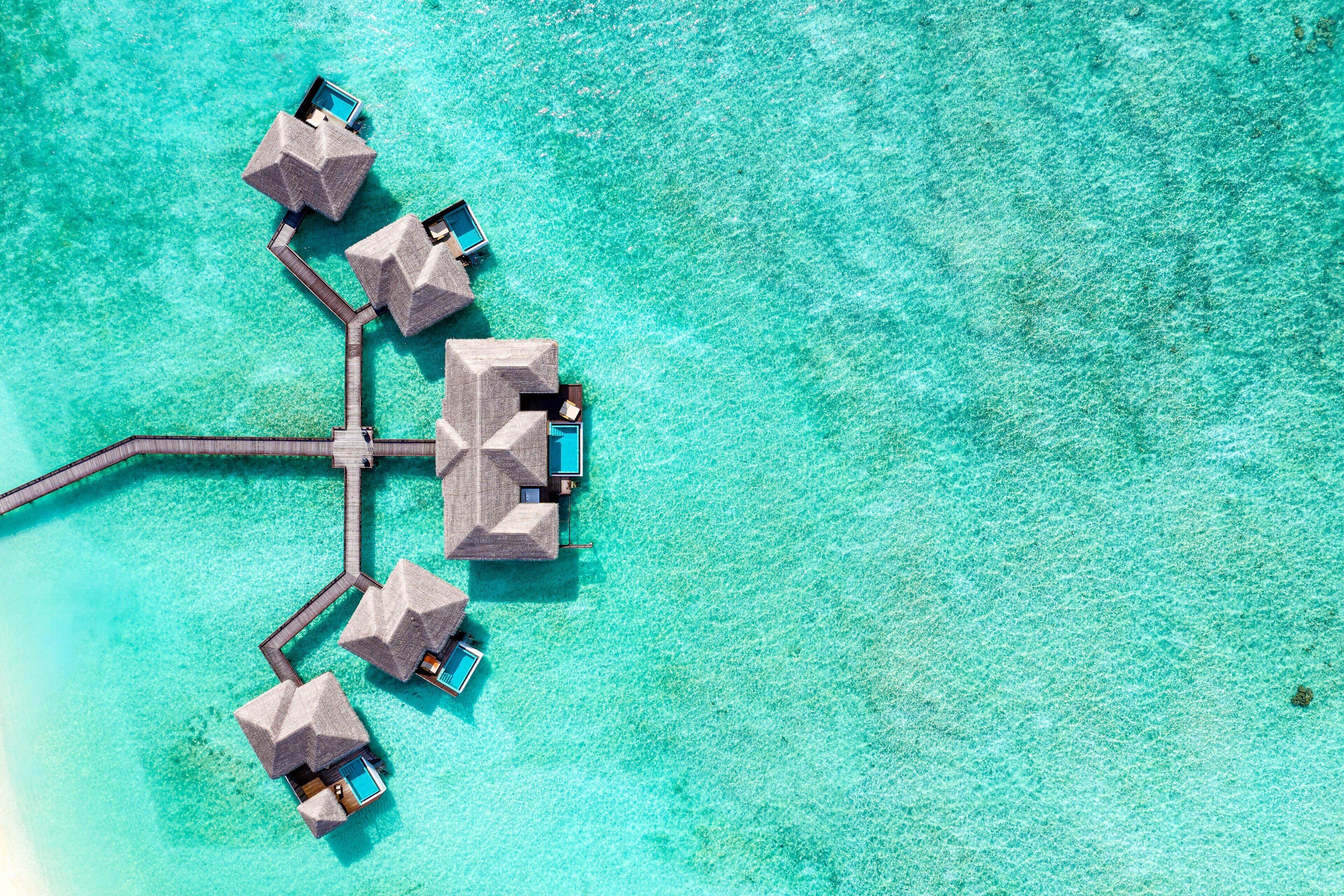 An aerial view of overwater bungalows connected by a dock, with clear turquoise water.
