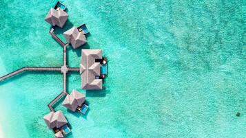 An aerial view of overwater bungalows connected by a dock, with clear turquoise water.