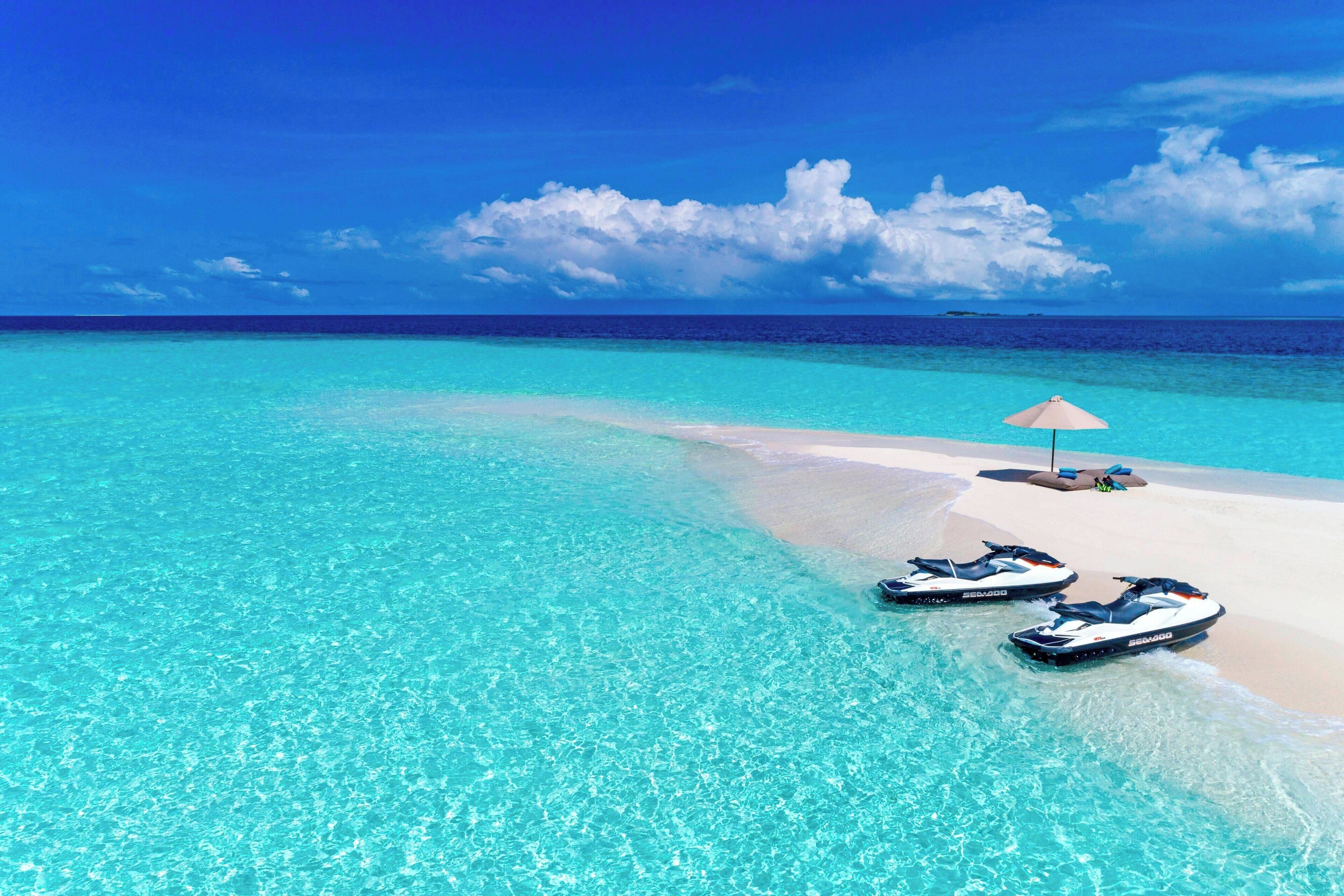 Une plage avec une eau turquoise et limpide, un rivage sablonneux et deux jet-skis.