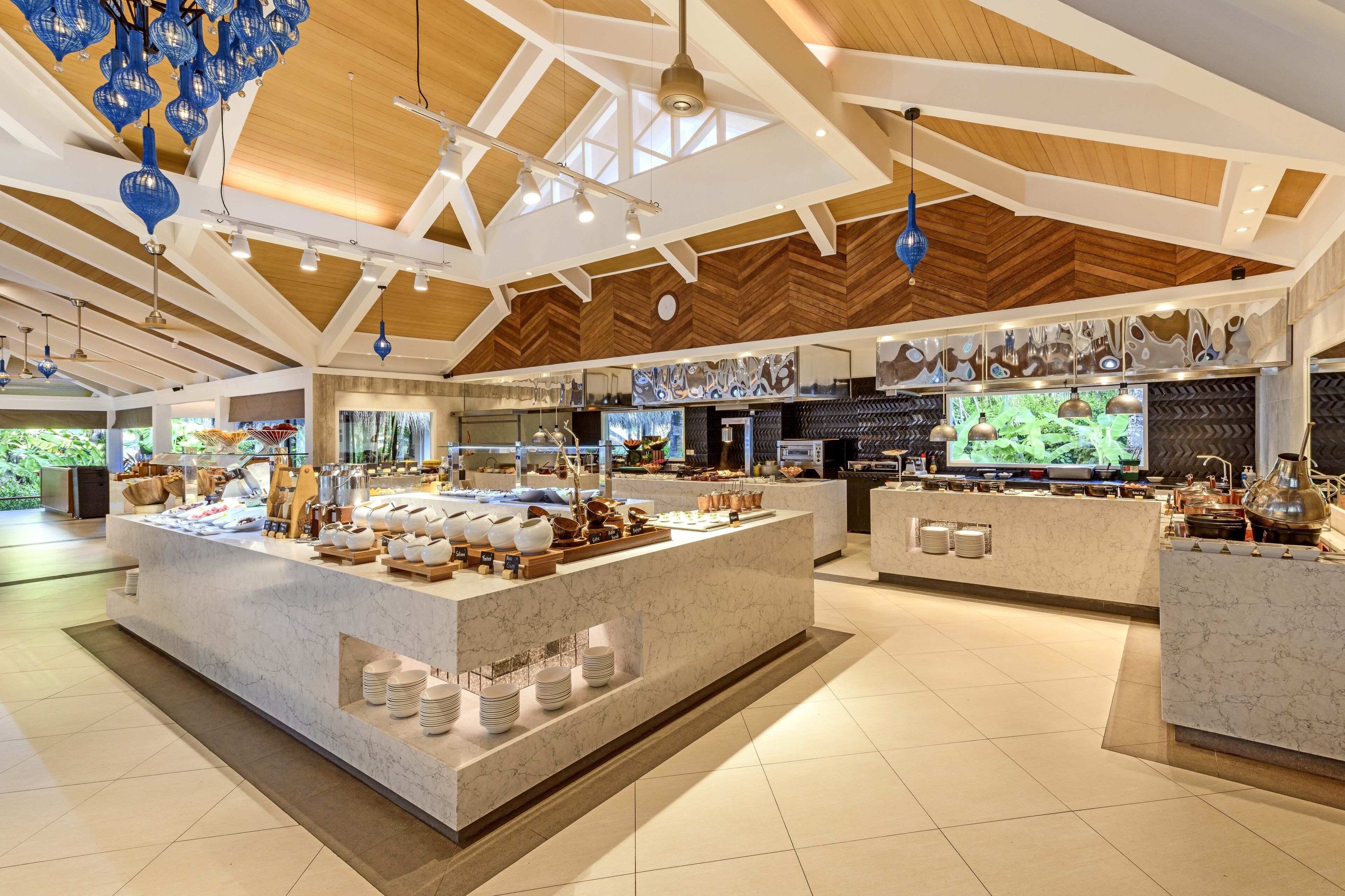 A spacious hotel lobby with a large marble reception desk, modern lighting fixtures, and a high ceiling with wooden beams.
