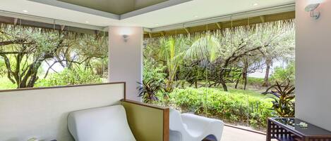 Una habitación moderna con un sofá blanco, una mesita pequeña y vistas a un jardín exuberante a través de amplios ventanales.