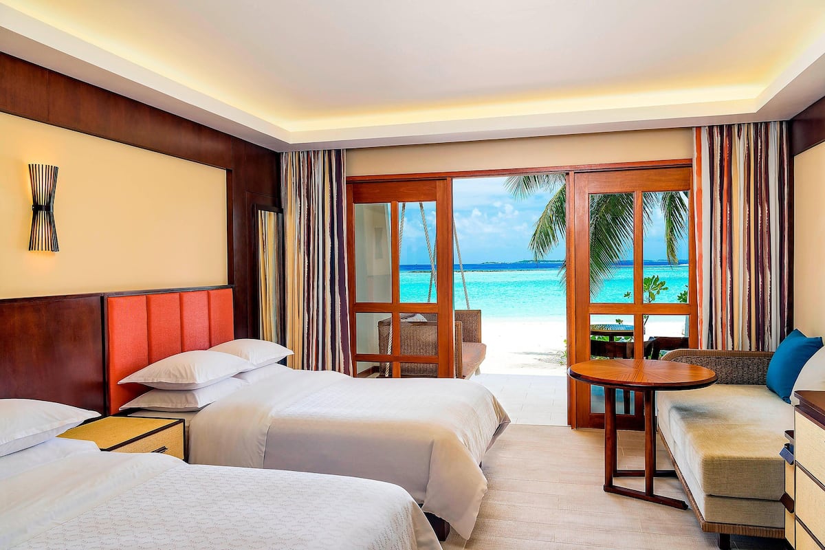 A hotel room with two beds, a wooden headboard, a small table, and a view of the ocean.