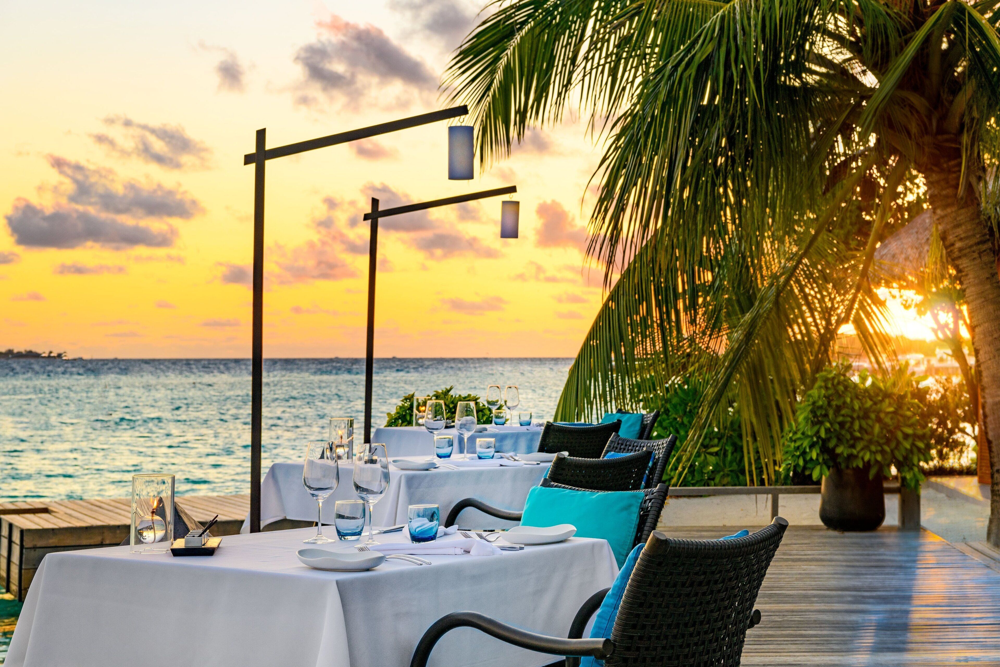 A table set for dining with a view of the ocean at sunset.