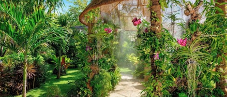 Un sendero en un jardín con una estructura de paja, rodeado de exuberantes plantas y flores tropicales.