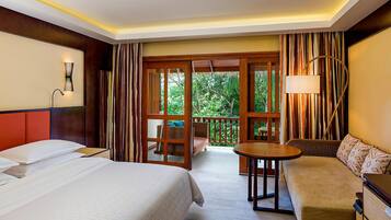 Une chambre d’hôtel avec deux lits, un canapé, une petite table et un balcon donnant sur un paysage verdoyant.