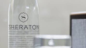 A clear glass bottle labeled 'SHERATON EST. 1937 PURE STILL WATER' on a marble surface.