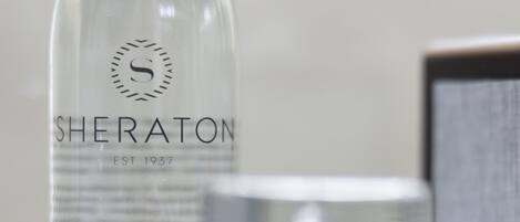 Una botella de vidrio transparente con la etiqueta 'SHERATON EST. 1937 PURE STILL WATER' sobre una superficie de mármol.