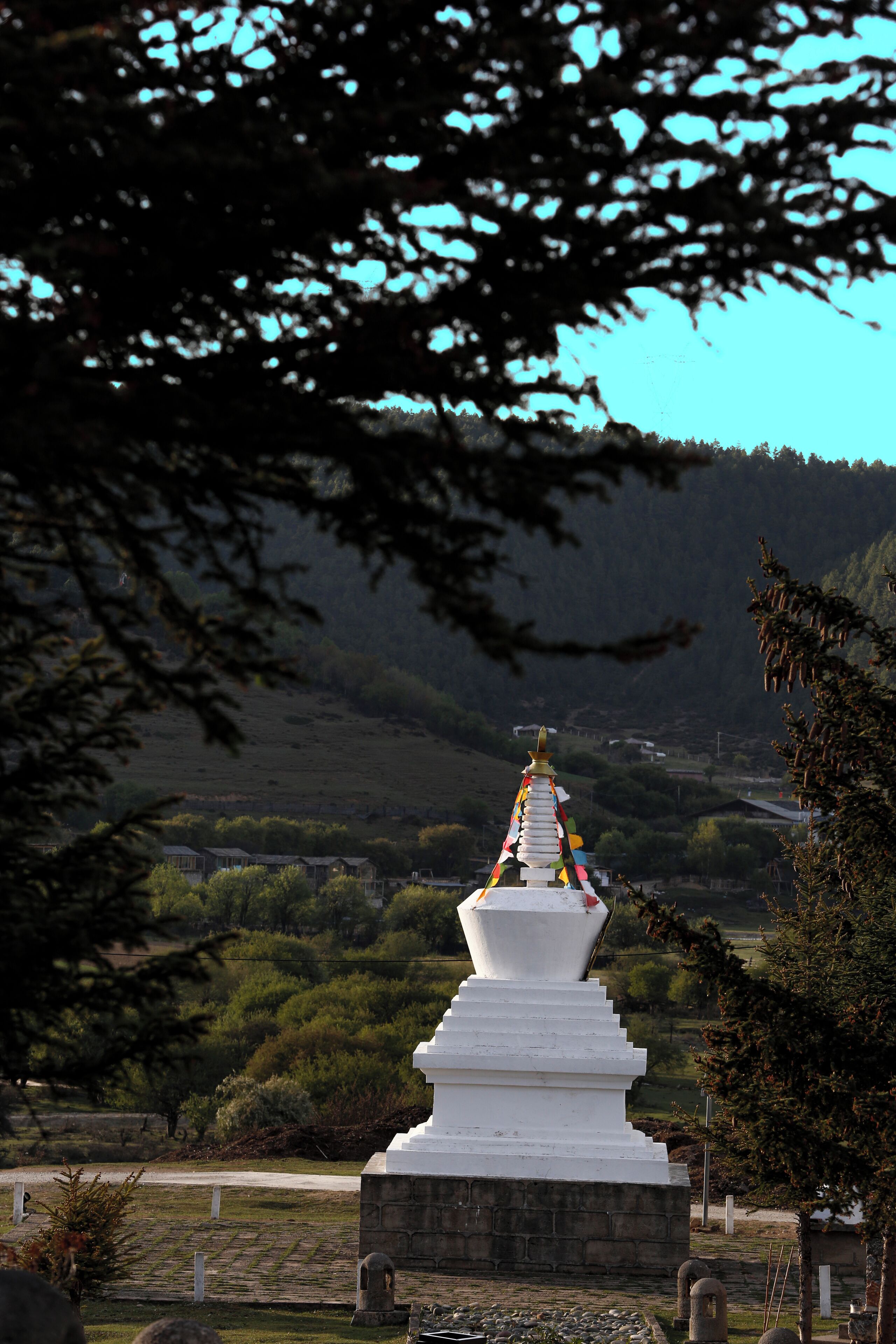 Una stupa blanca con oraciones en banderas de colores, rodeada de vegetación y un paisaje montañoso.