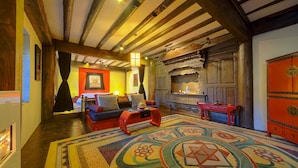 A cozy room with exposed wooden beams, a colorful patterned rug, a sofa, and a red cabinet. - Banyan Tree Ringha (Deqin)