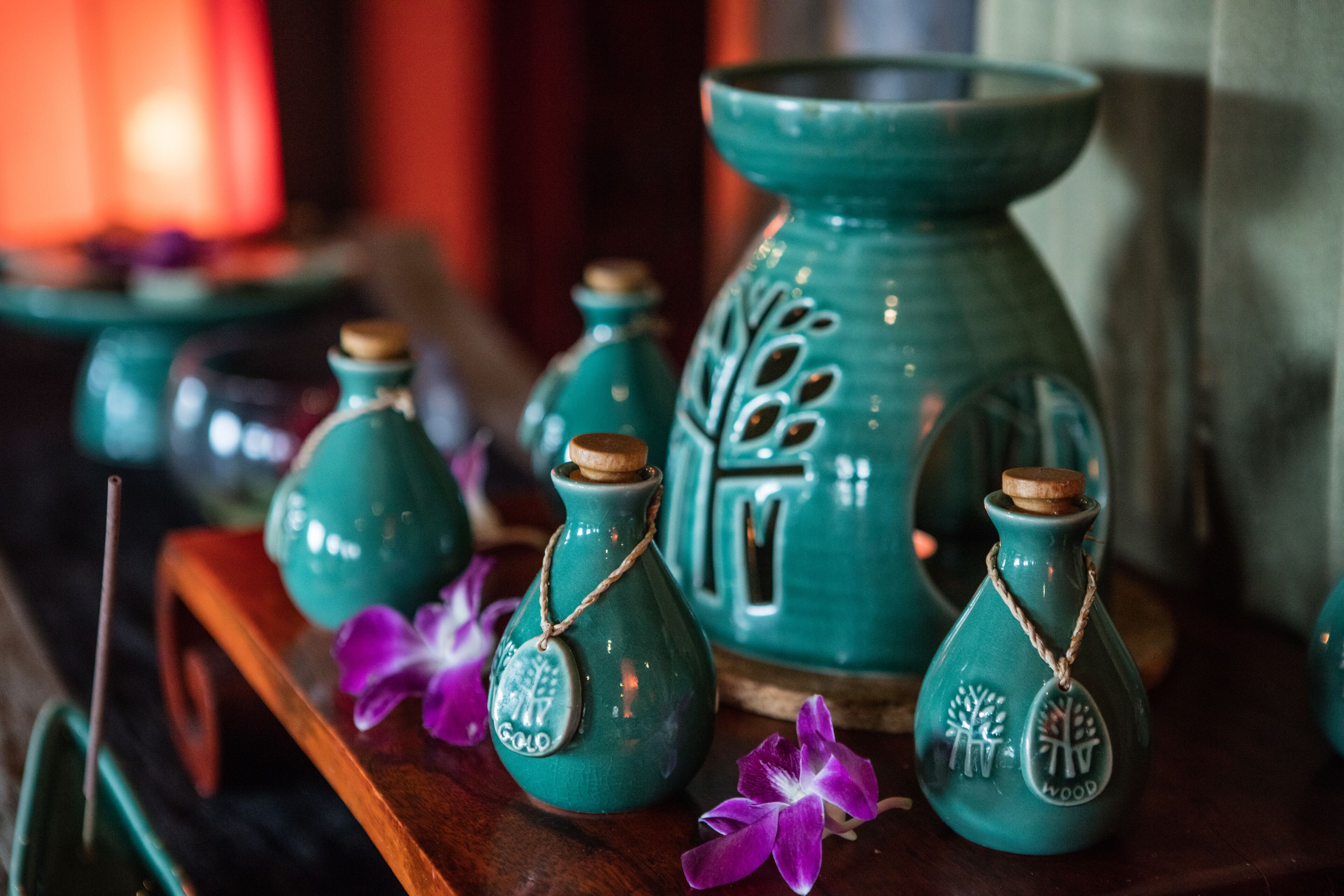A collection of teal ceramic vases with cork stoppers and wooden tags, displayed on a wooden surface with purple flowers.