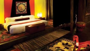 A hotel room with a bed, a nightstand, a lamp, a decorative tapestry, and a red chair. - Banyan Tree Ringha (Deqin)