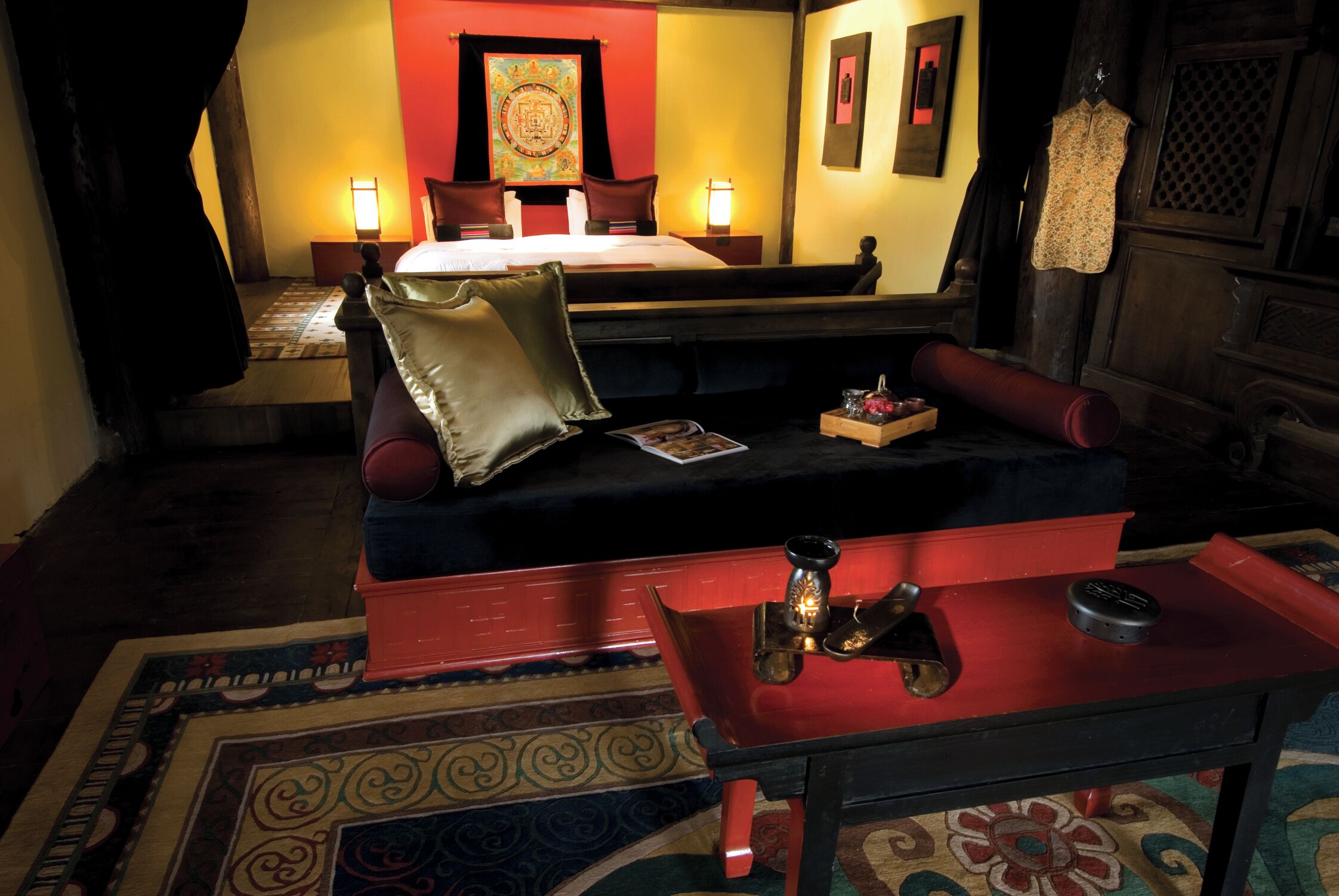 A hotel room with a bed, a sofa, a small table with a lamp, and a decorative wall hanging.