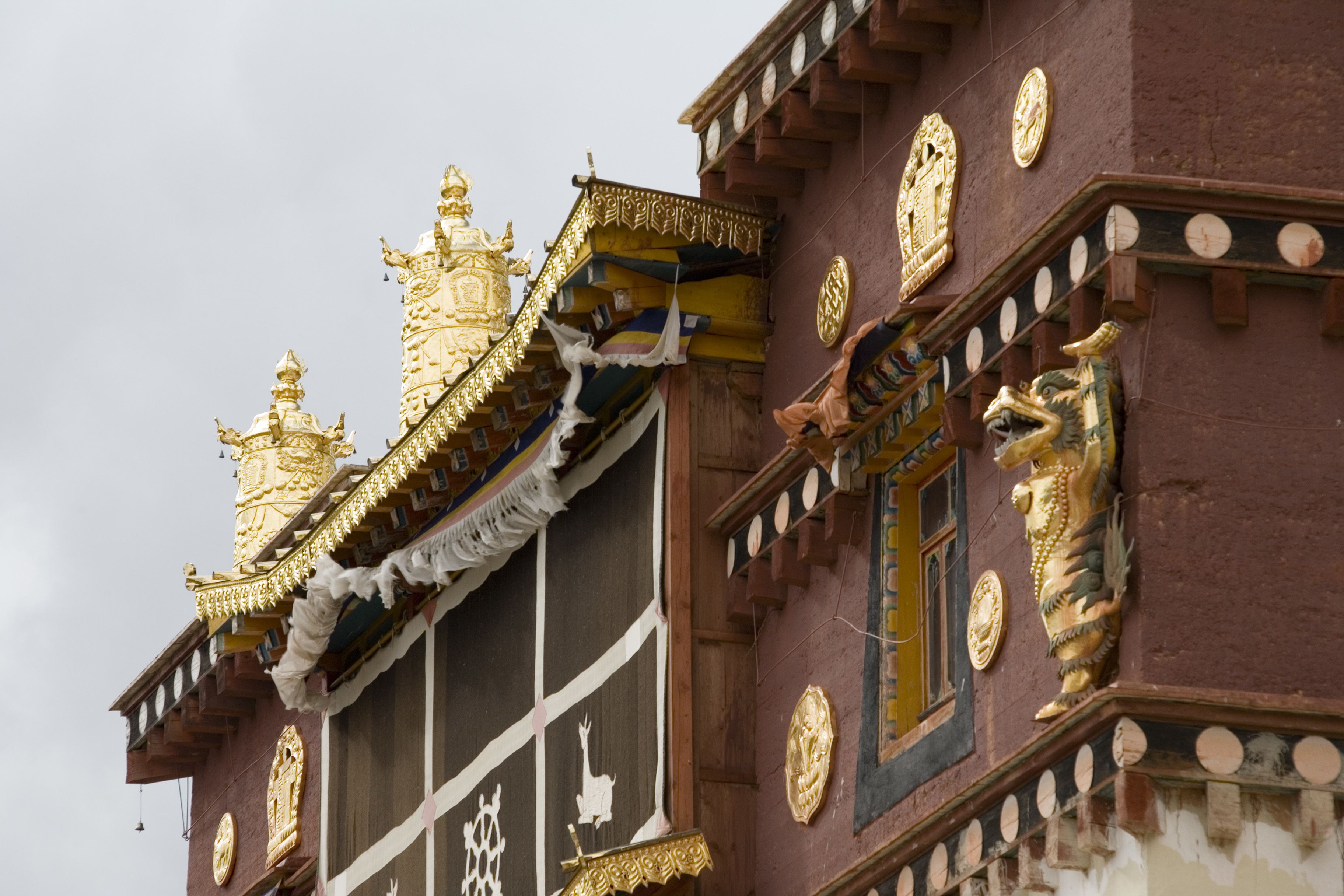 Un edificio tradicional con decoraciones doradas ornamentales, una ventana con marco decorativo y una estatua de criatura mítica.