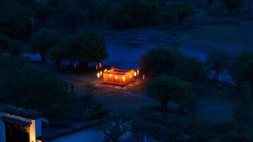 A small, illuminated structure surrounded by trees, likely a guest house or lodge, with a pathway leading to it.